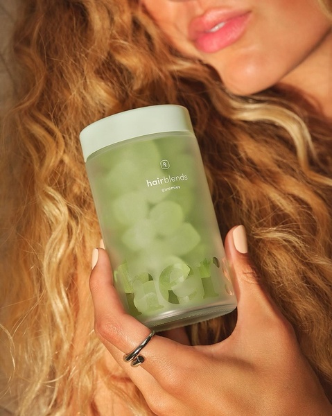 A close-up, high-quality product shot of Hair Blends Gummies held against a soft, textured background, focusing on brand clarity and product texture.